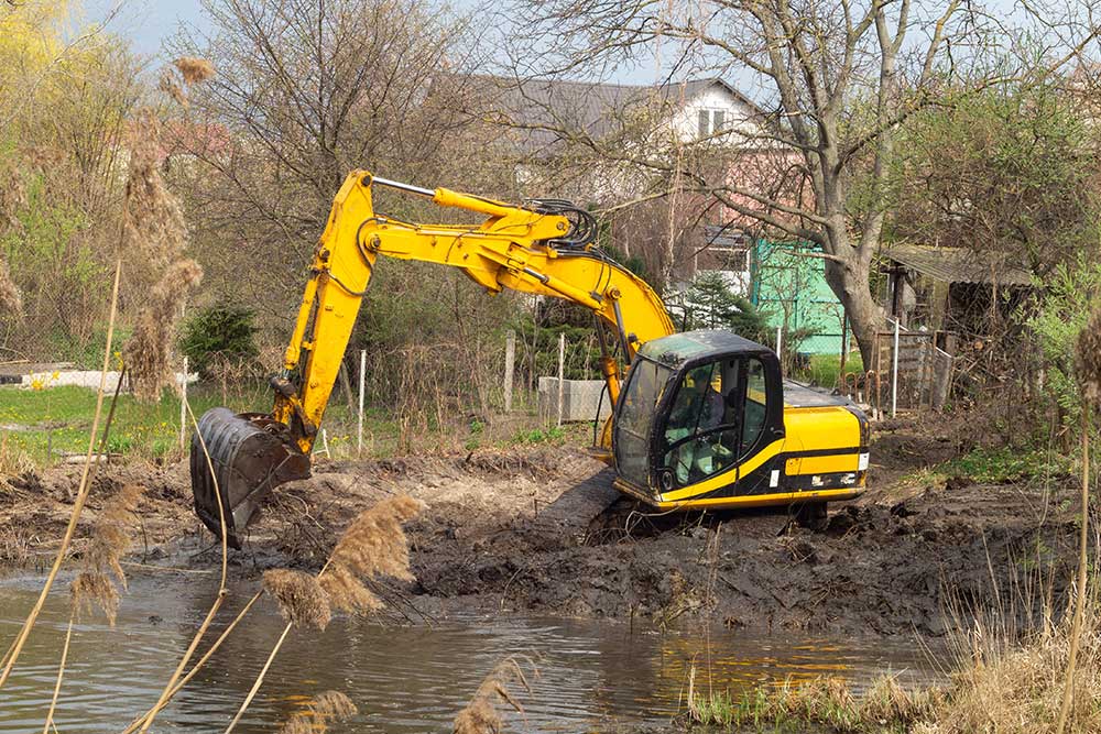 Crawler excavator or digger dredges on the lake. Deepens the bottom of the lake, moves soil to shore with a bucket